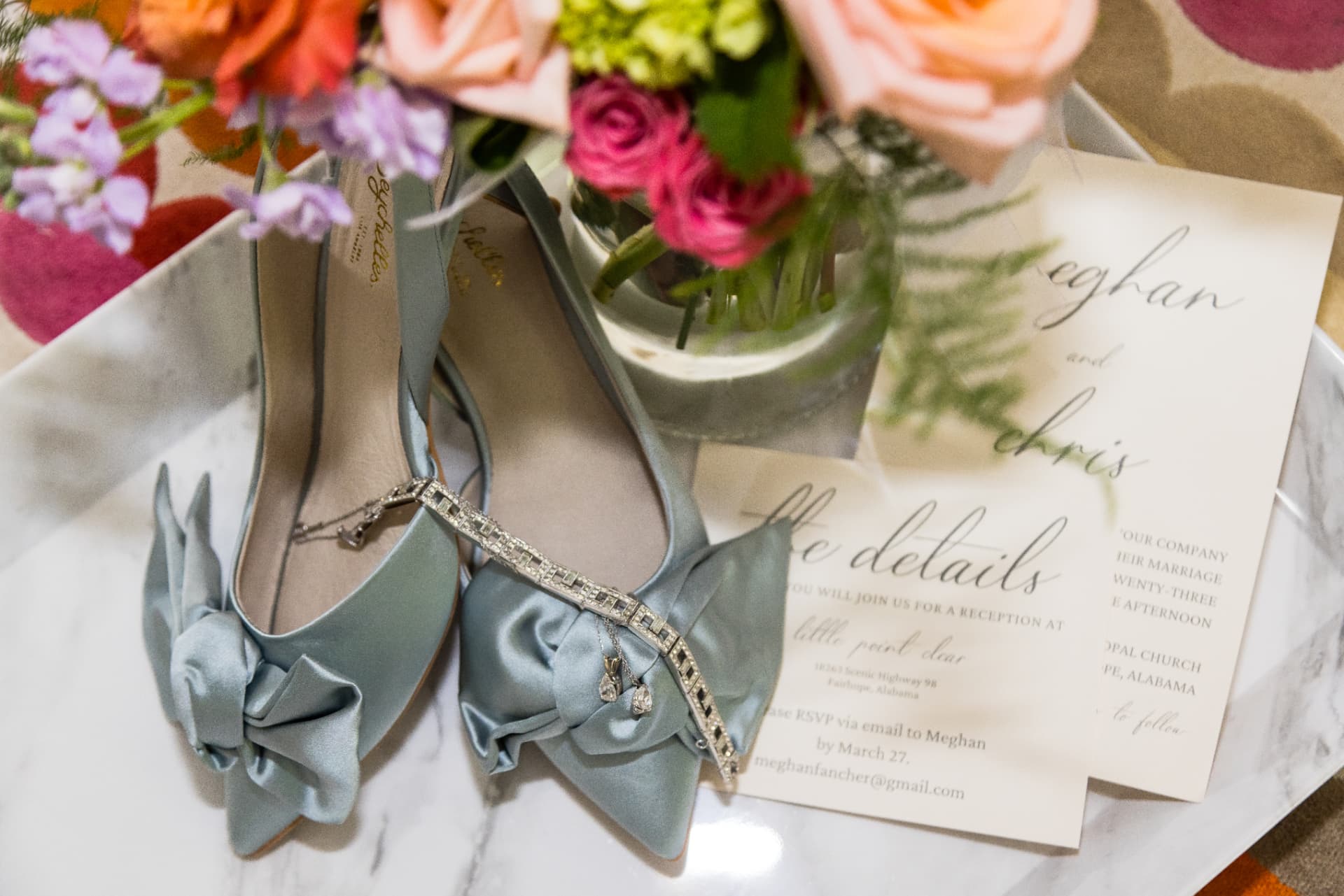 Wedding shoes, jewelry, invitation and flowers arranged on a marble table