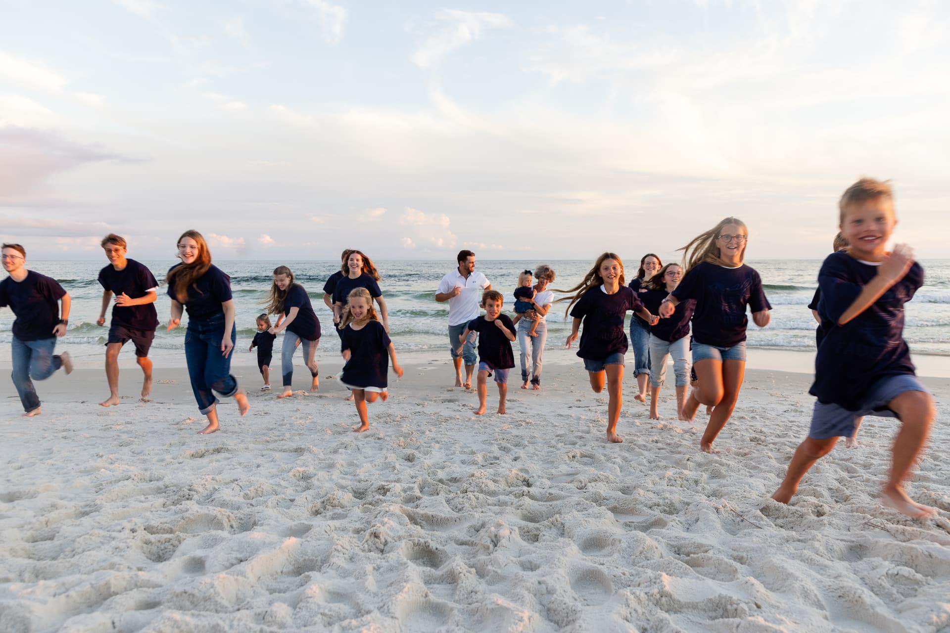 A large family running barefoot together across the sand at sunset